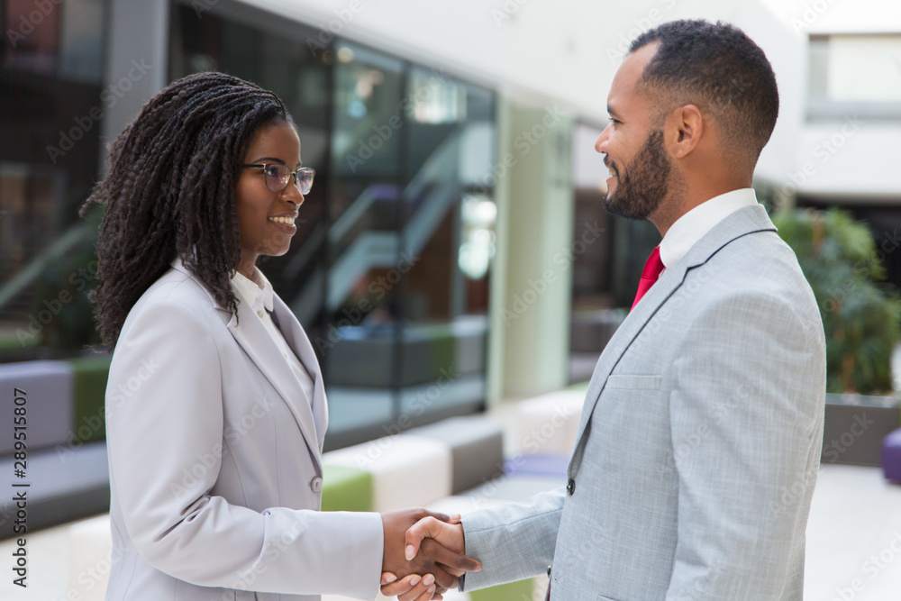 Happy successful business people greeting each other in office hallway. Business man and woman standing and shaking hands. Handshake concept