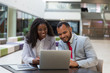 © Mangostar - Smiling business colleagues using laptop. Cheerful young African American business people sitting at table and using digital devices. Technology concept