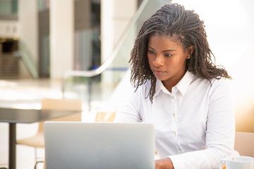 Wall Mural - Focused female employee working in cafe. African American business woman using laptop in public space. Wireless technology concept