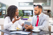 © Mangostar - Businessman showing project presentation to female colleague. Diverse business man and woman sitting in cafe, using tablet together and talking. Digital communication concept