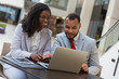 © Mangostar - Cheerful business colleagues using laptop. Smiling young African American business people sitting at table and using digital devices. Technology concept