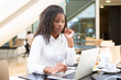 © Mangostar - Focused female office worker using computer in coffee shop. African American business woman working on laptop in cafe and looking away. Internet technology concept