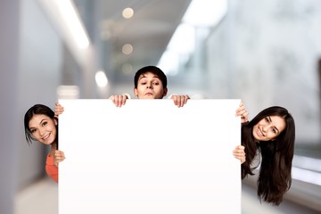 Canvas Print - Group of diverse multiethnic happy young people posing with a blank white rectabgular sign with copyspace for your advertisement or text on a grey background