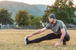 © _KUBE_ - Sports and yoga. A man with a beard, in sportswear performs stretching on the grass before training. Copy space