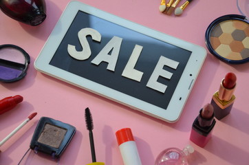 Different types of decorative cosmetics, next to a tablet with the words sale. Online Shopping Concept. Overhead view of Tablet and essential beauty items, Top view of female fashion accessories