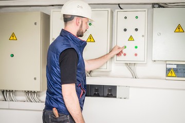 Wall Mural - An electrician in a helmet presses the control panel buttons. The specialist works with powerful electric boxes. Engineer checks the electrical supply system.