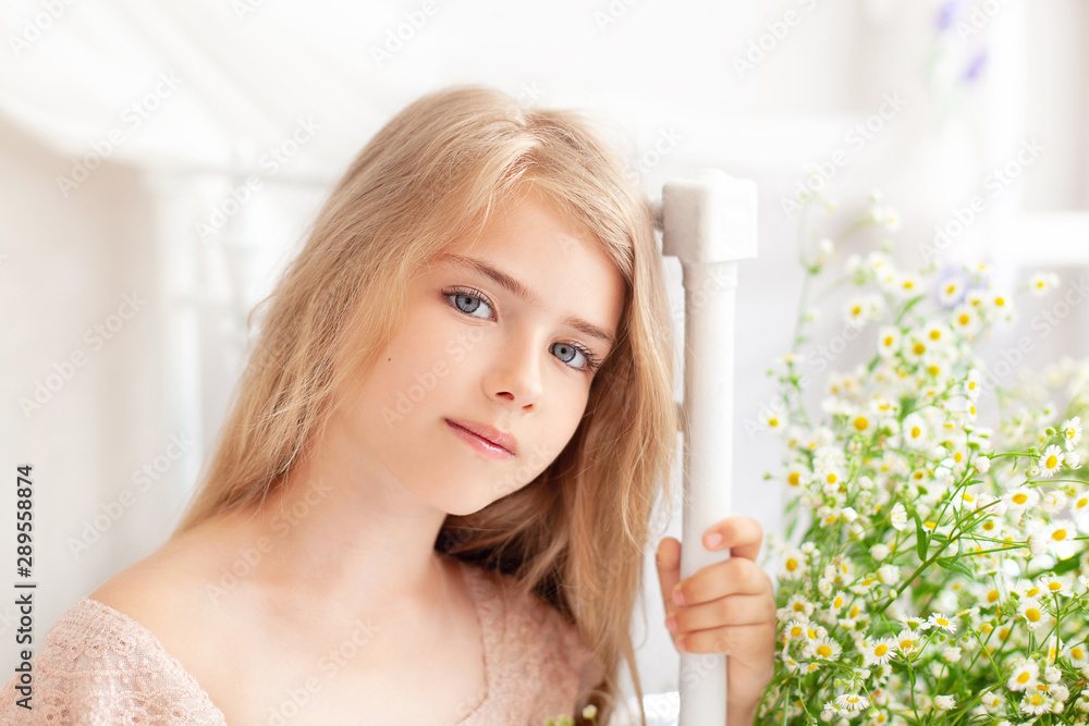 Beautiful little blonde girl with long hair sits on a bed with a ...