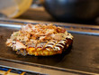 Closeup macro detail of a freshly cooked Okonomiyaki with Katsuobushi, dried fish flakes, sauce, and mayonnaise, on a Teppan grill. Shallow focus. Dotonbori, Osaka, Japan. Travel and cuisine.