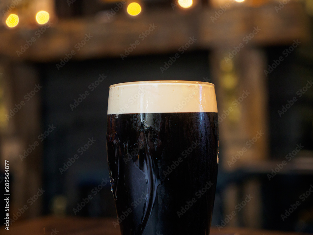 Close-up detail of a glass of cold stout lager in a traditional British pub. Windsor, United Kingdom. Drinks and cuisine. - obrazy, fototapety, plakaty 