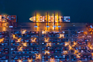 Aerial top view of container cargo ship in the export and import business and logistics international goods in urban city. Shipping to the harbor by crane in Victoria Harbour, Hong Kong City at night.