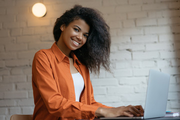 Wall Mural - Freelancer typing on keyboard using laptop computer. Portrait of cheerful woman copywriter working project in office. Smiling African American student studying, learning language. Online education