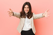 © Asier - Young brunette business woman against a pink background feels confident giving a hug to the camera.