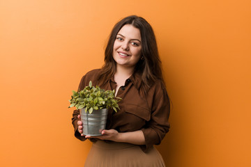 Wall Mural - Young curvy plus size woman holding a plant happy, smiling and cheerful.