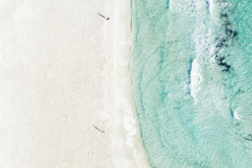 View from above, stunning aerial view of two people walking a white beach bathed by a beautiful turquoise clear water. Emerald Coast (Costa Smeralda) Sardinia, Italy.