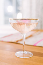 Romantic Pink Bubbly Sparkling Cocktail Made With Champagne, Vodka, And Rose Water, Shaken With Ice, Served In Gold Rimmed Coupe Glass, Garnished With Rose Petal.
