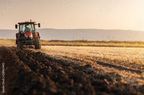 Fotomural Tractor plowing fields in sunset