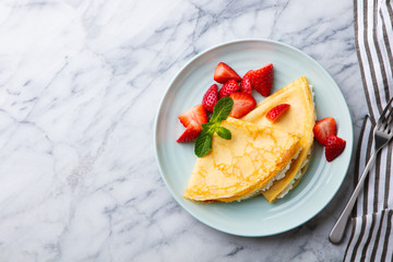 Wall Mural - Crepes, thin pancakes with cream cheese, ricotta and fresh strawberries. Marble background. Top view. Copy space.