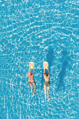 Top view of two women swimming in the pool on a sunny day.