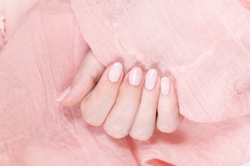 Wall Mural - Closeup view of one beautiful female hand isolated on soft pink fabric texture background. Fingers with fresh pastel nude look manicure at short oval nails. Trend of natural beauty concept.