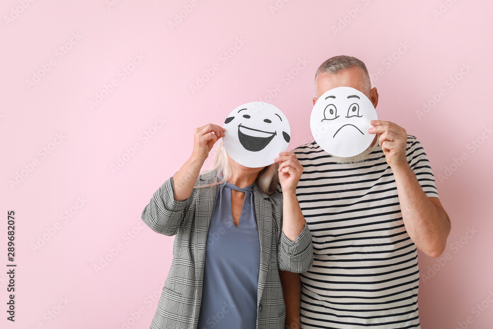 Mature couple hiding faces behind emoticons on color background