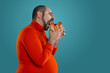 © nazarovsergey - Close-up portrait of a middle-aged man with beard, dressed in a red turtleneck, posing with burgers against a blue background. Fast food.