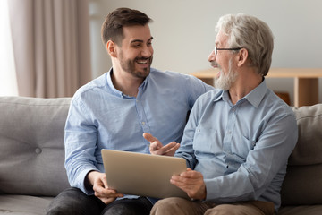 Wall Mural - Happy excited old father and young son talking using laptop