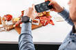 © Carlo Prearo - top view with the focus on the background of tapas and appetizers arranged on a white table while a person takes a picture using a mobile phone. foodie, social network, and trend concepts