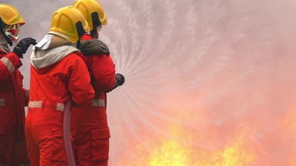 Wall Mural - Slow motion wide shot firefighter in safety fire suit rescue extinguishing crackle fire flames inside burning premises. Three fireman teamwork using water extinguisher from a hose for fighting a fire