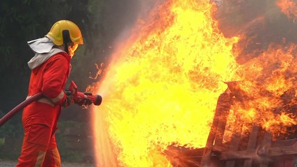 Wall Mural - HD Slow motion medium shot of firefighter in fire suit on safety rescue duty using water extinguisher from a hose extinguishing crackle fire flames inside burning premises. Fireman fighting a fire.