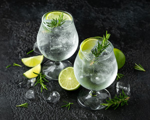 Wall Mural - Gin and Tonic Alcohol drink with Lime, Rosemary and ice on rustic black table