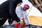 Fototapeta Uliczki - Arabic woman and her husband pouring oil in the car engine