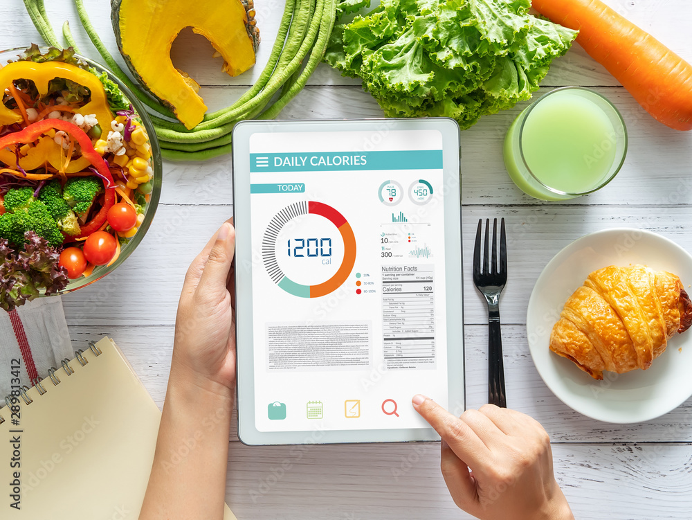 Calories counting , diet , food control and weight loss concept. woman using Calorie counter application on tablet at dining table with fresh vegetable salad - obrazy, fototapety, plakaty 