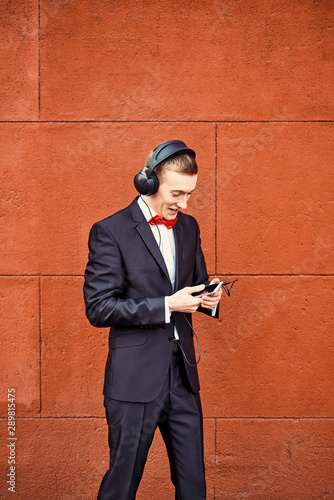 Young Guy In A Black Suit White Shirt And A Red Bow Tie A Man In Big Headphones Listening To Music In The Background Of Burgundy Wall Stock Photo Adobe Stock