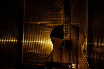 Wall Mural - An wooden acoustic guitar is against a grunge textured wall. The room is dark with a spotlight for your copyspace.