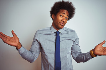 Sticker - American business man with afro hair wearing shirt and tie over isolated white background clueless and confused expression with arms and hands raised. Doubt concept.