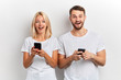 © alfa27 - Photo of beautiful excited happy man and woman with wide open mouth smiling while both using smart phones isolated over white background. happiness, positive feeling and emotion, sale discount