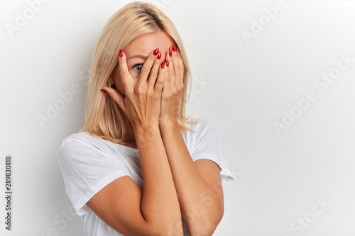 Fotomural young fair-haired girl covering face with hands, her eyes full of terror and pan