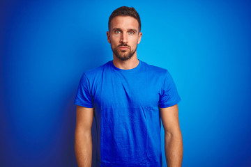 Sticker - Young handsome man wearing casual t-shirt over blue isolated background Relaxed with serious expression on face. Simple and natural looking at the camera.