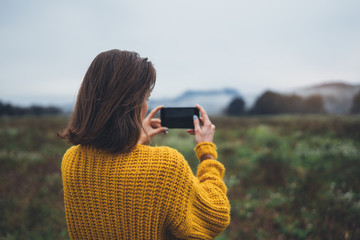 photographer girl hold in hands mobile phone taking photo on smartphone autumn froggy mountain, tourist shooting on photo camera on background landscape