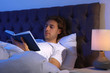 © New Africa - Handsome young man reading book in dark room at night. Bedtime