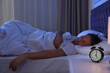 © New Africa - Alarm clock on nightstand near sleeping young man. Bedtime