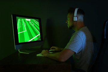 Canvas Print - Man with headphones playing video game on modern computer in dark room