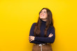 Teenager girl over isolated yellow wall looking up while smiling