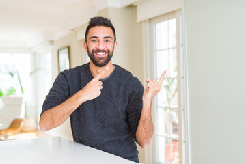 Sticker - Handsome hispanic man wearing casual sweater at home smiling and looking at the camera pointing with two hands and fingers to the side.