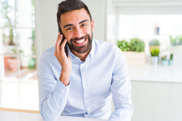 Poster - Handsome hispanic business man having a conversation talking on smartphone with a happy face standing and smiling with a confident smile showing teeth