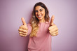 © Krakenimages.com - Young beautiful woman wearing a sweater over pink isolated background success sign doing positive gesture with hand, thumbs up smiling and happy. Cheerful expression and winner gesture.