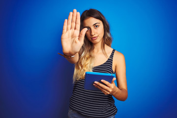 Canvas Print - Young beautiful woman using touchpad tablet over blue isolated background with open hand doing stop sign with serious and confident expression, defense gesture