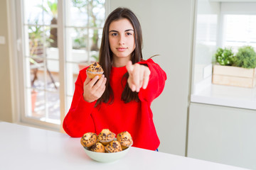 Canvas Print - Beautiful young woman eating chocolate chips muffins pointing with finger to the camera and to you, hand sign, positive and confident gesture from the front