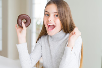 Wall Mural - Beautiful young girl wearing eating a chocolate donut screaming proud and celebrating victory and success very excited, cheering emotion