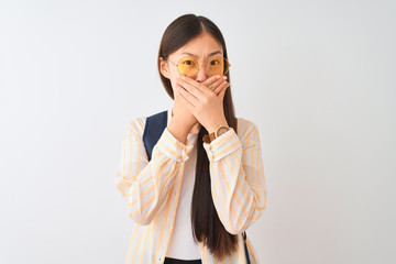 Sticker - Young chinese student woman wearing glasses and backpack over isolated white background shocked covering mouth with hands for mistake. Secret concept.